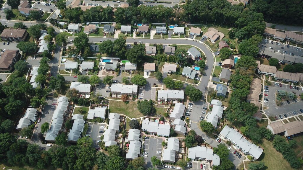 Aerial view of a suburban neighborhood with rows of houses, trees, parked cars, and curved streets.