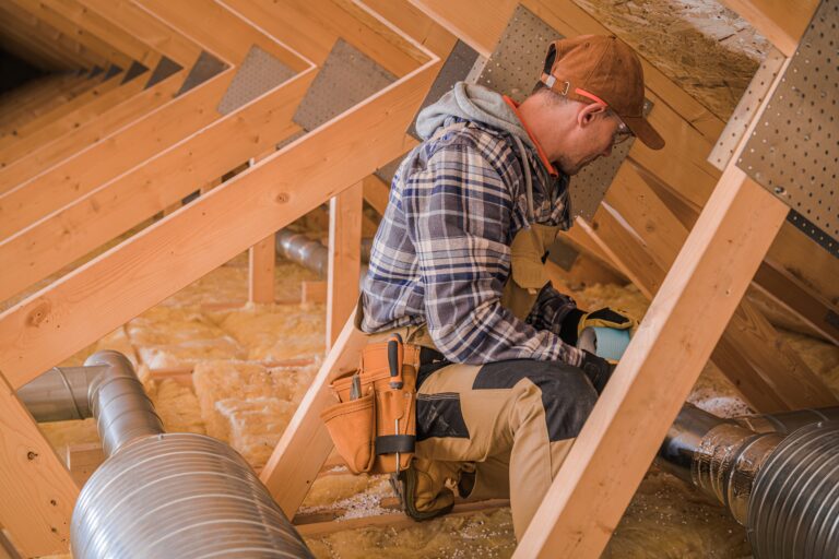 A worker in a plaid shirt and work overalls installs or inspects metal ductwork in an unfinished attic—reminding every home buyer budget planner about potential hidden costs when buying a home in Florida.