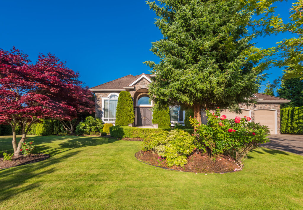 Single-story brick house with arched entry, surrounded by green lawn, shrubs, and trees—one of the 10 ways to boost your home’s curb appeal before listing is showcasing a well-maintained exterior on a clear sunny day.