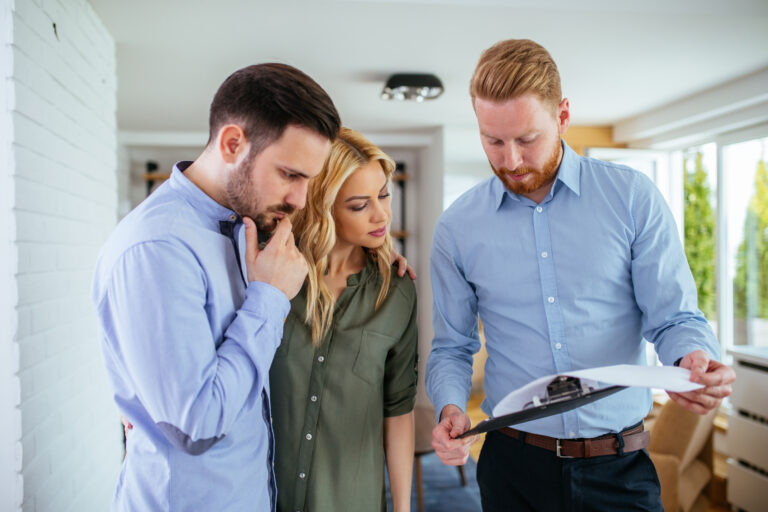 A man shows a clipboard with documents to a couple standing beside him in St. Cloud, all focused on reviewing the Home Inspections paperwork and discussing what's included indoors.