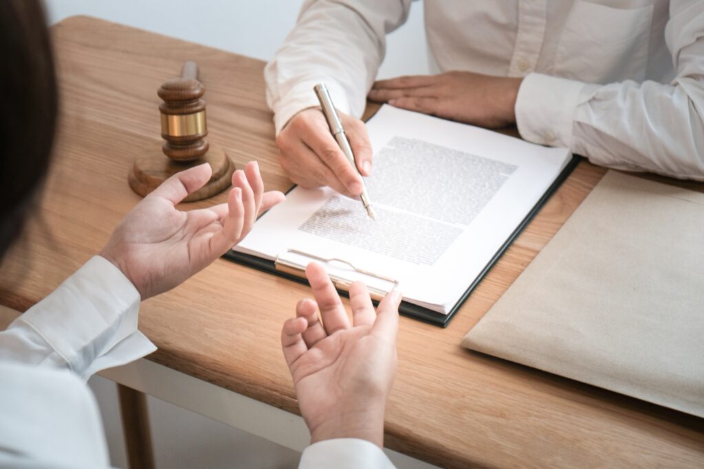 Two people sit at a desk with a legal document, gavel, and envelope; one points to the document while discussing St. Cloud real estate and who pays closing costs, as the other gestures with their hands.