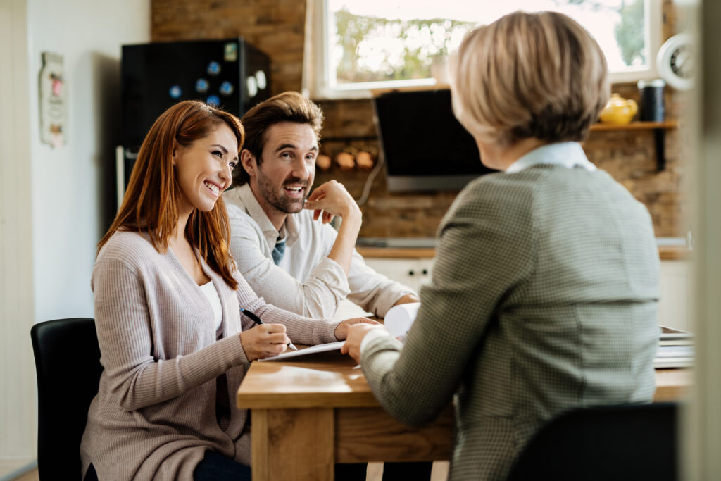 A woman and man sit at a table across from another woman in an office or home setting, engaged in conversation and paperwork as they discuss home buying options and the importance of getting pre-approved before beginning their house hunting journey.